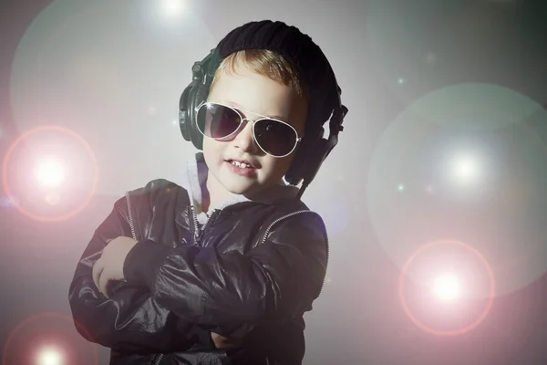 Pequeño DJ. niño divertido en gafas de sol y auriculares. Niño sonriente escuchando música en auriculares. DJ. discoteca luces —  Fotos de Stock