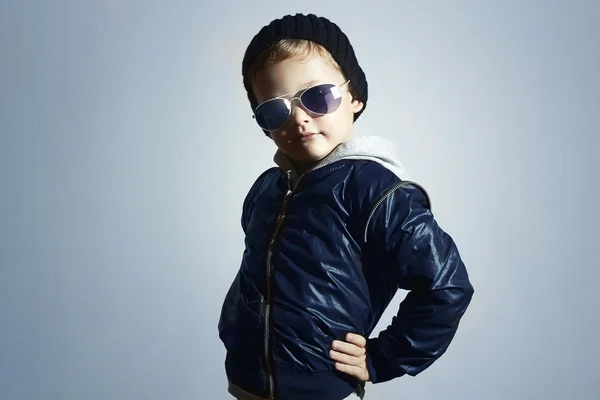Moda çocuk güneş gözlüğü. Siyah cap.winter tarzında evlat. Küçük çocuk poz. Çocuk moda. Mavi arka plan