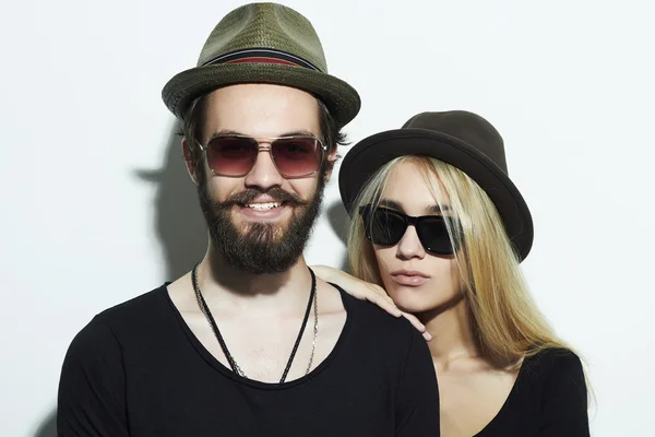 Belo casal feliz em chapéu vestindo óculos da moda juntos. Rapaz e rapariga hipster. Barbudo jovem e loira em óculos de sol — Fotografia de Stock