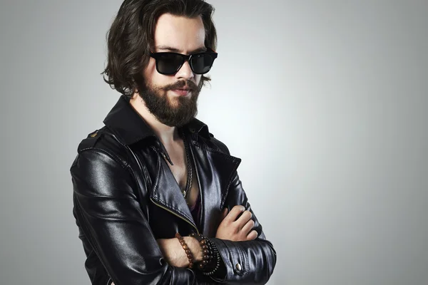 Hombre guapo de moda en una chaqueta de cuero. Muchacho sexy barbudo brutal en gafas de sol de moda.rock and roll — Foto de Stock