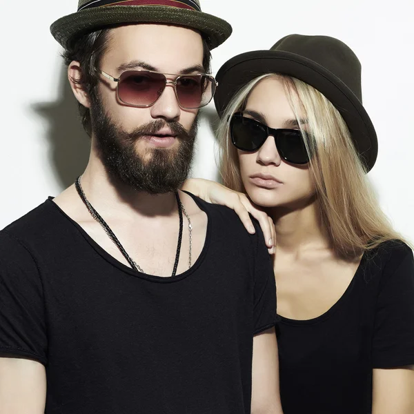 Bella coppia felice in cappello indossando occhiali alla moda insieme. Ragazzo e ragazza hipster. Barbuto giovane uomo e bionda in occhiali da sole — Foto Stock