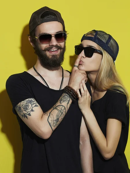 Moda hermosa pareja juntos. Tatuaje Hipster chico y chica. Joven barbudo y rubia en gafas de sol.Fondo amarillo — Foto de Stock