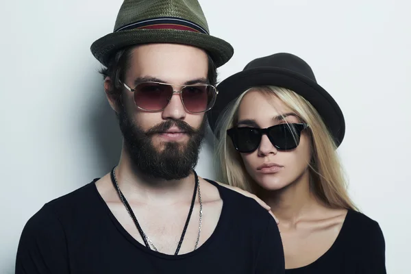 Moda hermosa pareja en sombrero juntos. Hipster chico y chica. Joven barbudo y rubia en gafas de sol —  Fotos de Stock