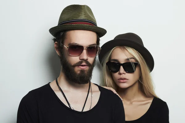 Hermosa pareja en sombrero con gafas de moda juntos. Hipster chico y chica. Joven barbudo y modelo rubia en gafas de sol —  Fotos de Stock