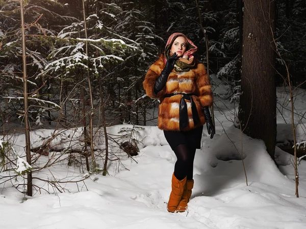 Beauty model girl in night winter forest. beautiful young Woman in fashionable Fur Coat and scarf.blond girl.snow around