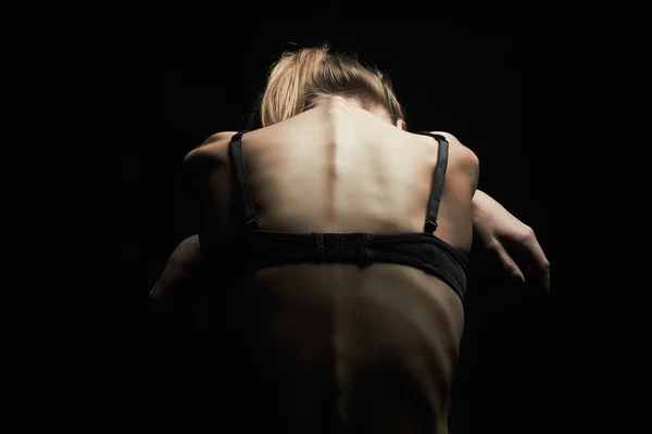 Sad young woman with naked back over black background — 스톡 사진