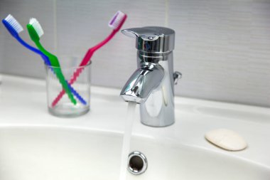 Diş fırçaları, sabun ve musluk musluğu beyaz banyo lavabosunda akan temiz suyla birlikte..
