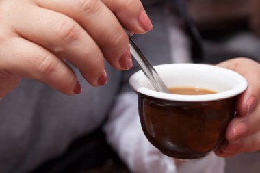 Sabah kahvesini ve sütünü küçük bir kaşıkla karıştıran bir kadın..