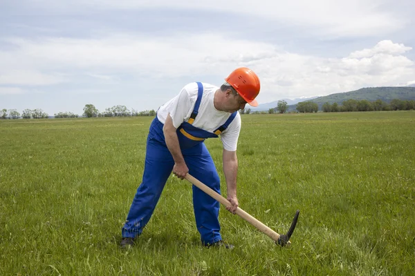 Працівник риття оглянуто pickaxe на зеленому полі — стокове фото