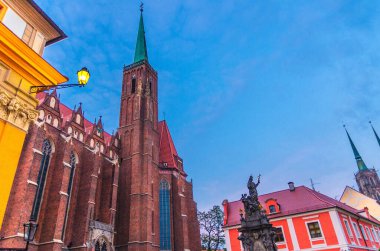 Tarihi şehir merkezi Ostrow Tumski, akşam manzarası, Wroclaw, Polonya 'da tarihi kuleye sahip Katolik Kutsal Haç Kilisesi ve St. Bartholomew binasındaki anıt ve sokak lambası.