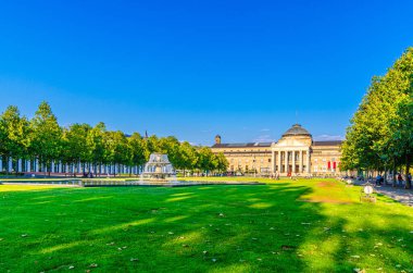 Wiesbaden, Almanya, 24 Ağustos 2019: Kurhaus or cure house spa and casino building and Bowling Green park with grass lawn, trees alley and lake with Fountain in history city center, State of Hesse
