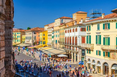 Verona, İtalya, 12 Eylül 2019: Tarihi kent merkezinde Piazza Sütyen Meydanı 'ndaki eski renkli binalar, çadırları ve yürüyen turistleri olan kafeler ve restoranlar, Veneto Bölgesi