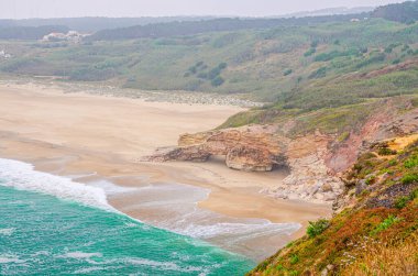 Atlantik Okyanusu 'nun, Nazare kasabası, Kuzey Sahili Praia do Norte, Leiria Bölgesi, Oeste Bölgesi, Portekiz yakınlarındaki kayalar ve uçurumlar ve gök mavisi turkuaz dalgaları ile kumlu sahilin üst hava manzarası.