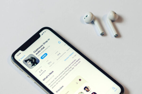 Minsk, Belarus, March 2, 2021: Clubhouse drop-in audio chat application view on smartphone screen and wireless earphones on white background, social network audio chat app on Apple s App Store
