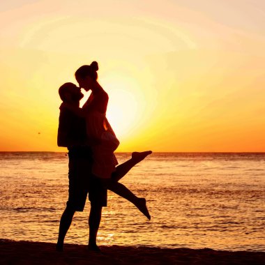 Sahilde romantik bir çift. Arka planda renkli bir günbatımı.