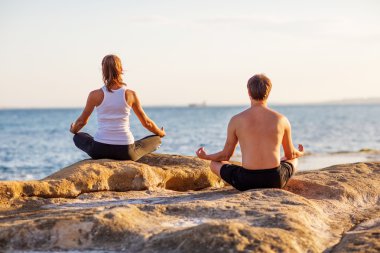 genç bir çift gün batımında sahilde Yoga uygulamak