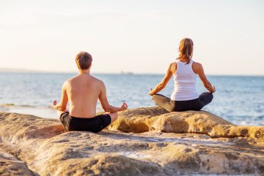 genç bir çift gün batımında sahilde Yoga uygulamak