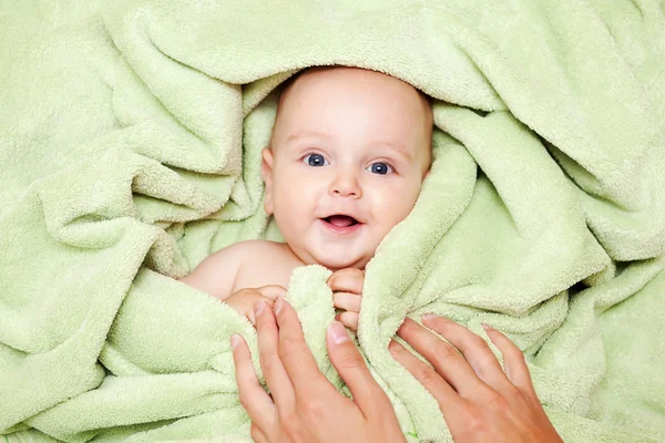 Caucasian baby boy covered with green towel joyfully smiles at c — Stock Photo, Image