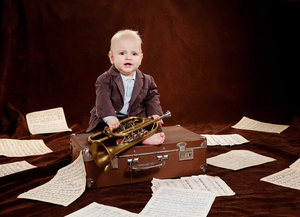 Caucasian baby boy plays with trumpet between sheets with musica Stock Image