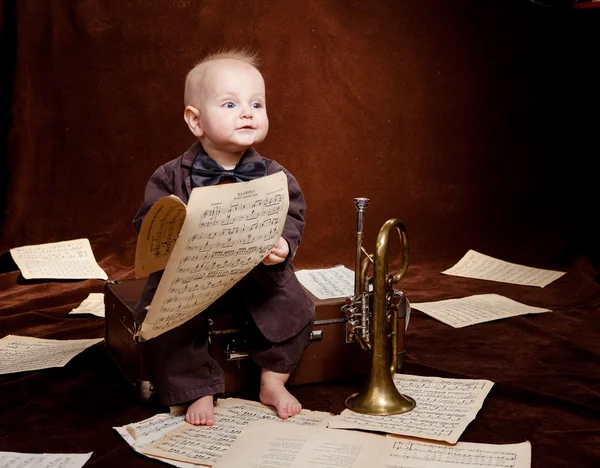 Caucasian baby boy plays with trumpet between sheets with musica Royalty Free Stock Images