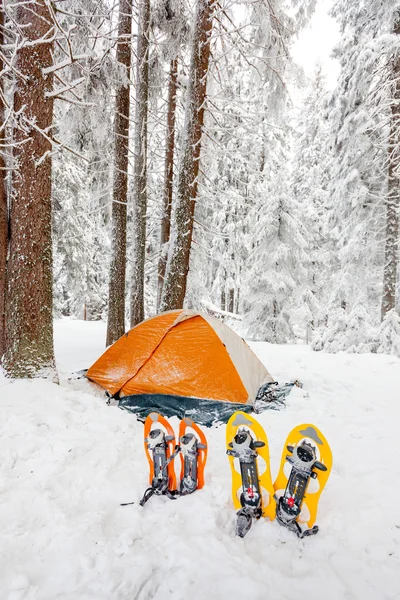 Χιονοπέδιλα αριστερά μπροστά από πορτοκαλί σκηνή στο δάσος του χειμώνα — Φωτογραφία Αρχείου