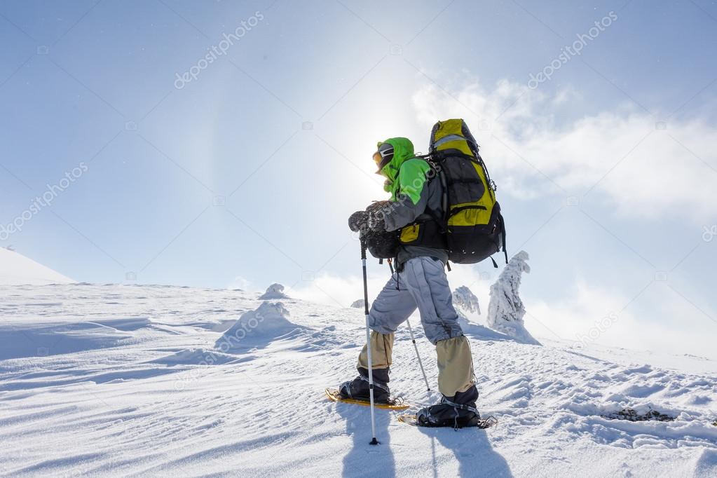 Backpacker man walking in winter mountains on sunny day