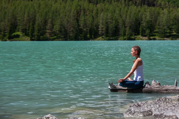 Mujer joven está practicando yoga en el lago de montaña —  Fotos de Stock