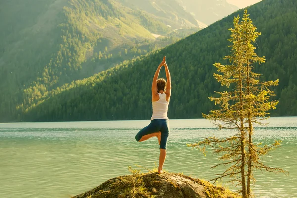 Young woman is practicing yoga at mountain lake — Stock Photo, Image