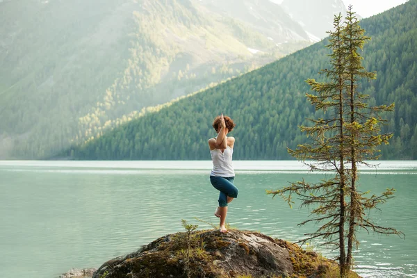 Mujer joven está practicando yoga en el lago de montaña — Foto de Stock