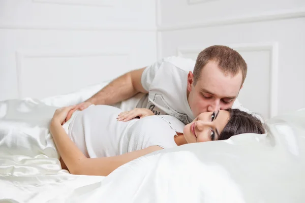 Happy pregnant family lies on the house bed. Stock Photo
