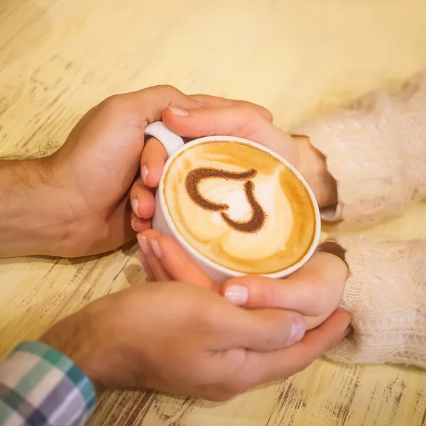 Fyra händer virad runt en kopp kaffe med hjärta ritning — Stockfoto