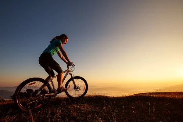 Biker-gadis di matahari terbenam di pegunungan — Stok Foto