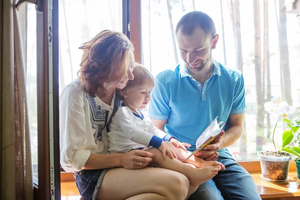 Família feliz sentado em um peitoril da janela e ler um livro . — Fotografia de Stock