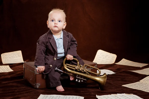 Caucasian baby boy plays with trumpet between sheets with musica Stock Picture