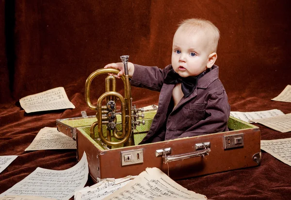 Caucasien bébé garçon joue avec trompette entre feuilles avec musica Photo De Stock