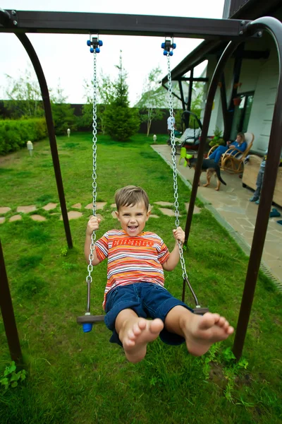 Pequeno menino caucasiano se diverte no swing ao ar livre — Fotografia de Stock