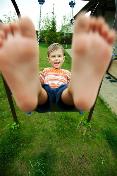 Pequeno menino caucasiano se diverte no swing ao ar livre — Fotografia de Stock