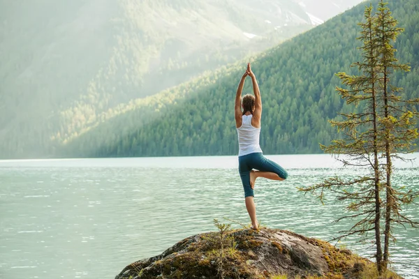 Young woman is practicing yoga at mountain lake — Stock Photo, Image