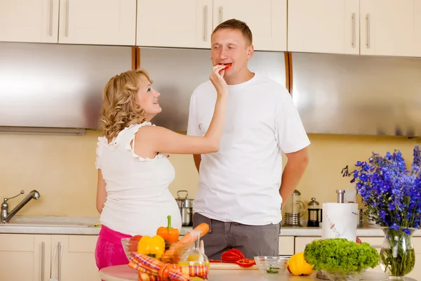 Jovem mulher grávida alimenta seu marido com legumes na cozinha — Fotografia de Stock