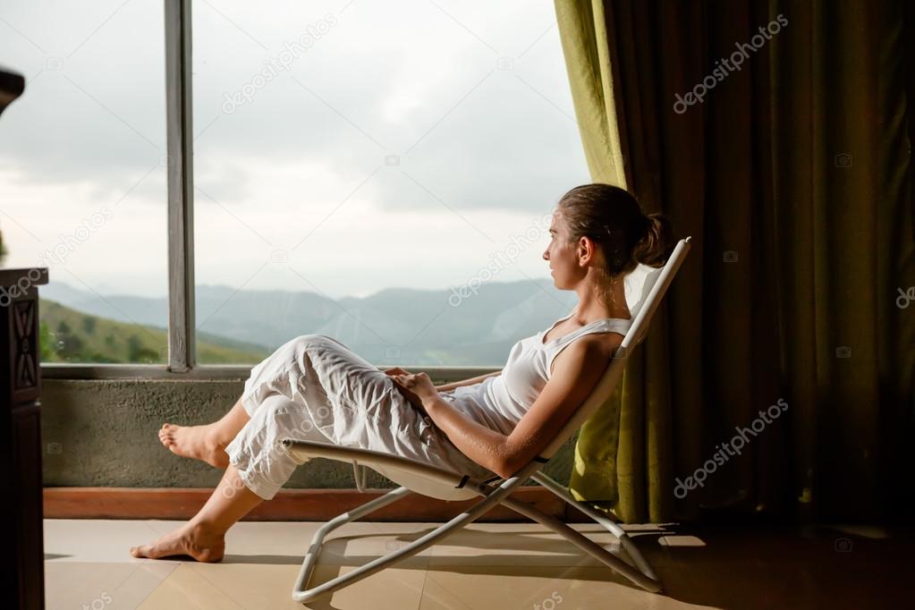 Woman is sitting in cozy armchair at hotel high up in mountains