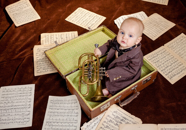 Caucasian baby boy plays with trumpet between sheets with musica