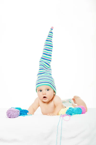 Caucasian cute boy in funny colorful hat between balls of yarn — Stock Photo, Image