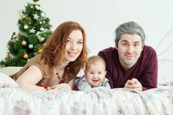 Familia feliz sentada en el árbol de año nuevo en el estudio blanco — Foto de Stock