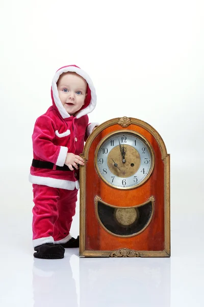 Small boy in Santa suit plays with vintage clock in white studio — Stock Photo, Image