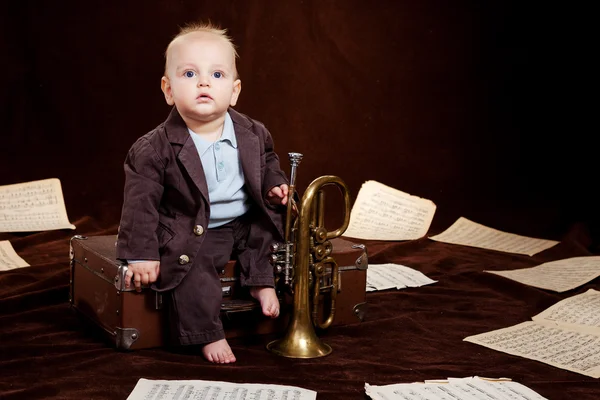 Caucasian baby boy plays with trumpet between sheets with musica Royalty Free Stock Photos