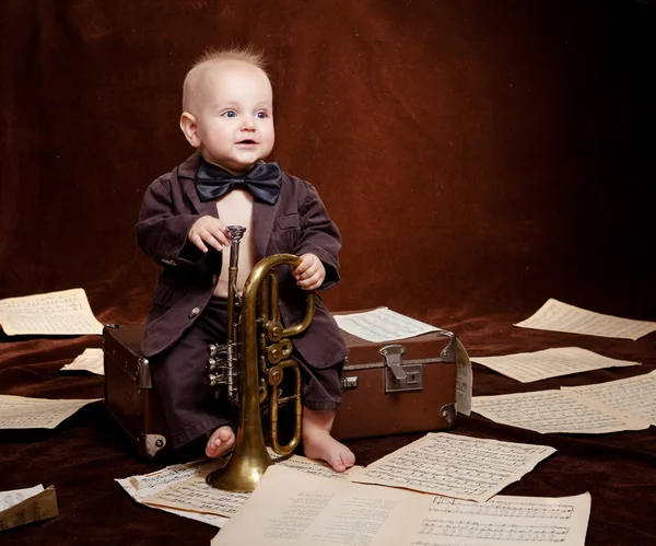 Caucasian baby boy plays with trumpet between sheets with musica Stock Photo