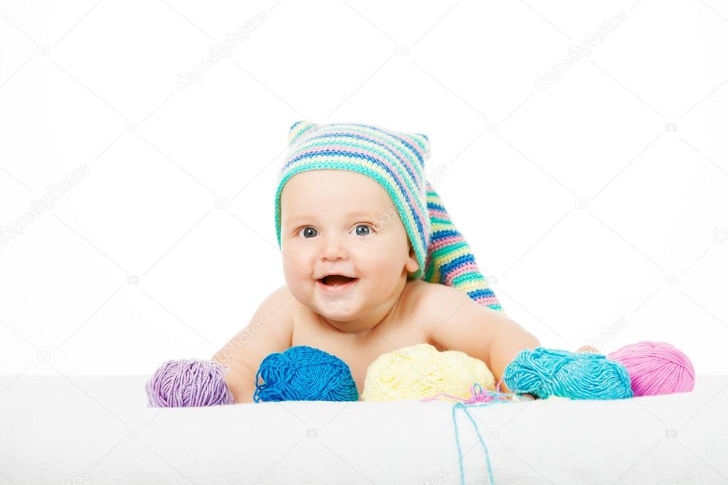 Caucasian cute boy in funny colorful hat between balls of yarn