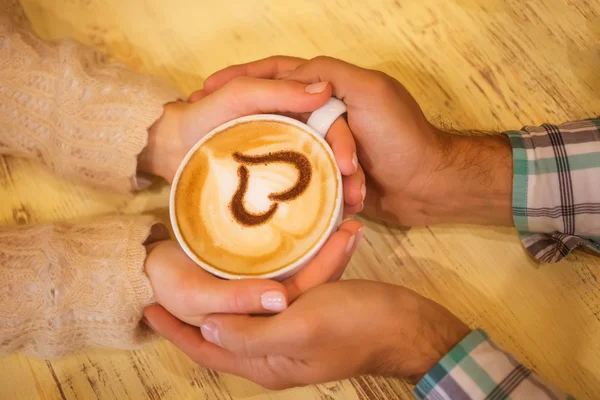 Quatro mãos enroladas em torno de uma xícara de café com desenho do coração — Fotografia de Stock