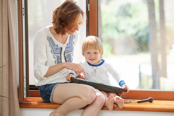 Familia feliz sentada en un alféizar de la ventana y leyendo un libro . — Foto de Stock