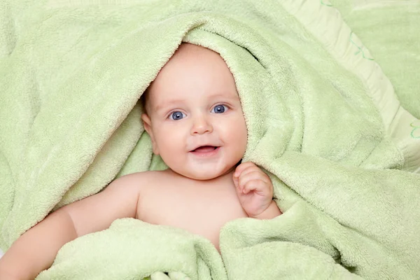 Caucasian baby boy covered with green towel joyfully smiles at c — Stock Photo, Image